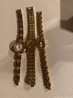 Three gold-tone ladies' wristwatches laid flat on a white surface showing front face and bracelet style.