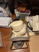 Off white hats stacked in a box on the floor with other packed household items