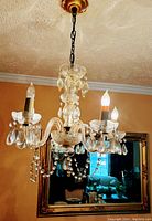 Vintage crystal glass chandelier hanging from ceiling, showing all five lit candle bulbs and crystal droplets.