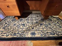 Top down photo showing the full width of the blue and cream wool area rug with Asian motif underneath wooden furniture.