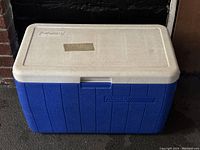 Blue and white Coleman cooler closed with visible logo and molded handles.