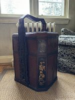 Front angled photo of the hexagonal wicker and lacquer Chinese food basket showing carved handle, painted panels, and woven texture.