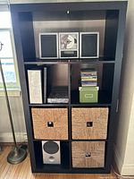 Front view of black/brown IKEA Expedit 2x4 cube bookcase filled with some baskets and items to show scale and use