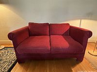 Front view of vintage red upholstered loveseat showing two seat cushions and two back cushions with padded scroll armrests.