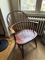 Front-left angle view of the wooden Windsor chair showing overall shape, seat, turned legs and loose finger piece underneath left armrest