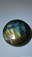 Close-up photo showing round labradorite gemstone with checkerboard facets capturing golden and blue flashes under lighting.