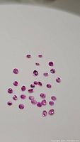 Top view of 32 natural pink sapphires in various vibrant pink shades arranged on a white background showing their round cut and clarity.