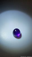 Clear detailed image of the smooth, round cabochon amethyst showing its deep purple color and glossy finish under focused lighting.