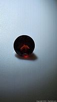 Photo of natural deep red garnet with round cut against a plain background showing its color and depth.