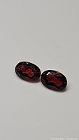 Pair of oval cut Mozambique garnet gemstones on neutral background, showing deep red facets.