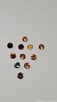 Photo showing 11 round faceted multicolored sapphires including orange, yellow, light blue, dark red, black, and coral shades.