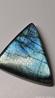 Close-up image of the polished trillion-shaped labradorite gemstone showing vibrant blue and golden flash.