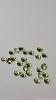 Photo of 28 small, round, calibrated apple green peridot gemstones scattered on a flat surface, showing their size, cut, and color.