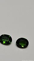 Pair of oval-shaped electric green chrome diopside gemstones with visible facets.