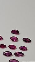 Close-up of several marquise cut rubies with exotic red to purple tones arranged on a grey background, showing facets and clarity.