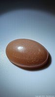 Large oval peach moonstone cabochon showing the smooth polished surface and sparkling inclusions.