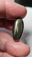 Close-up of natural pyrite oval cabochon gemstone held between fingers showing the golden metallic luster and smooth polished surface.