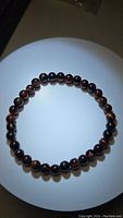 Round polished natural red tigerseye beads arranged on a stretchy elastic band forming a bracelet, glowing under focused light showing bead colors and patterns.
