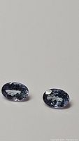 Pair of natural blue oval cut tanzanite gemstones on a plain surface, showing color and clarity