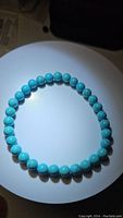 Top down photo of natural turquoise bracelet showing round beads arranged in circle on white background under spotlight.