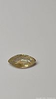 Single marquis cut yellow-greenish sapphire gemstone lying flat on a light surface, showing faceting and clarity.