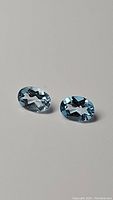 Two oval cut sky blue topaz gemstones shown against a plain background with clear lighting to display their transparency and color.