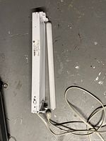 White rectangular tube lighting fixture with a 24 inch fluorescent tube and attached plug-in cord.