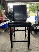 Front view of one brown wooden kitchen bar chair with black cushioned seat and backrest, showing footrest bar and condition.