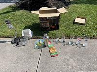 Photo showing all items including six beer glasses, plastic bottle markers, metal ice bucket, glass wine aerator and holder, cocktail shaker, and wine stopper arranged outdoors.