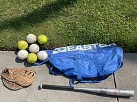 Full lot overview showing seven balls (four yellow softballs, three white baseballs), catchers mitt, 31-inch metal bat, and blue Easton bag on concrete near grass.