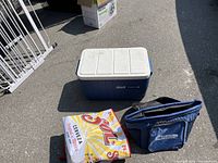 Three coolers including one hard sided blue and white Coleman PolyLite 34 cooler and two soft sided coolers, one Curtis brand blue soft cooler bag and one smaller dark soft cooler bag, outdoors on asphalt.
