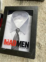 Season Two DVD box of Mad Men series showing a white shirt and tie on the cover, boxed set in black case.