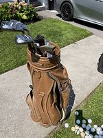 Golf clubs in brown leather golf bag with golf balls on ground