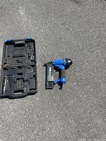 Mastercraft air nailer and open black plastic storage case shown outside on asphalt.