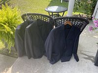 Three men's suit jackets shown on chairs outdoors, colors dark gray, black, and navy