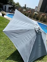Grey patio umbrella canopy spread open outside near a pool, showing fabric and panels.