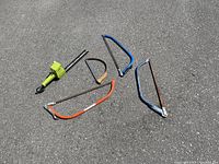 Wide shot of the electric hedge trimmer and four handheld pruning saws laid on asphalt, showing all tools in the lot.