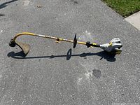 Full side view of Ryobi gas trimmer showing curved yellow shaft, engine housing, handle, and protective guard.