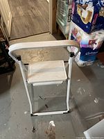 Front view of the small foldable step ladder, showing white metal frame and single step with wear marks on textured surface.