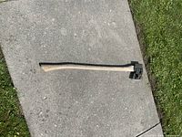 Full view of the long-handled wooden axe with metal splitting head lying on concrete