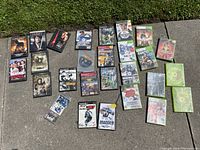 Full spread of multiple Xbox and Playstation 2 games along with several DVD movies laid out on the ground.