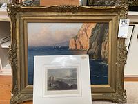 Framed coastal painting leaning against shelf with matted steel engraving print placed in front