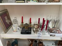 Shelf view showing four crystal candle holders with red tapers, small votive holder, brass inkwell on marble base, silver bear figurine, and two pewter-stem wine glasses