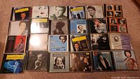 Several rows of music CDs with classical and pop/rock artists arranged flat on carpet.