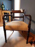 Front-facing image of vintage wood chair showing upholstery and carved wooden arms and legs.