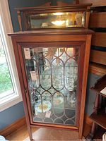 Frontal view of wood china cabinet showing decorative glass door with fretwork and internal shelves