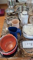 Assorted kitchen items including plastic mixing bowls, measuring pitcher, insulated carafe, stainless cookware and glass bakeware on countertop