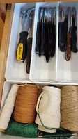 Top drawer view showing Roland opener, hand file, black-handled serrated knives and twine spools