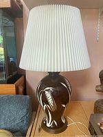 Front view of the lamp showing the brown porcelain body with white decoration and pleated white lampshade.