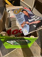 Cardboard box filled with GQ magazines, top issue shows Liam Neeson cover